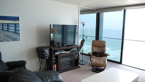 A living room with a TV, a leather couch, a white coffee table, and a view of the ocean through large windows. - ONE BEDROOM CONDO 706 (San Diego)