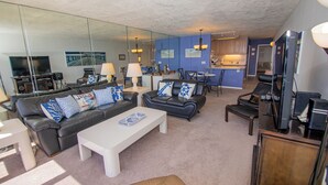 A living room with a sofa, coffee table, and chairs. There is a kitchen area with a dining table and chairs. - ONE BEDROOM CONDO 706 (San Diego)