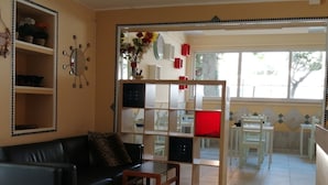 A living room with a black sofa, a wooden coffee table, and a glass partition with shelves. There are potted plants on a shelf and a window with a view of the outside. - BRENNERO  (Rimini)