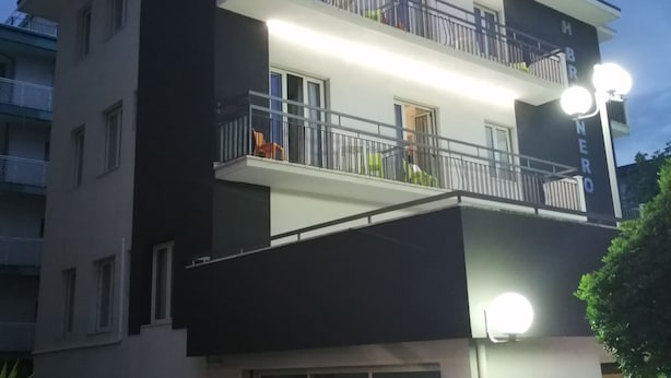 A multi-story hotel with balconies, a sign indicating a meeting point, and a well-lit facade. - BRENNERO  (Rimini)
