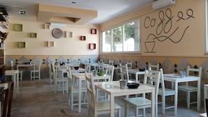 A dining area with white tables and chairs, a clock, and a wall with a coffee cup design. - BRENNERO  (Rimini)