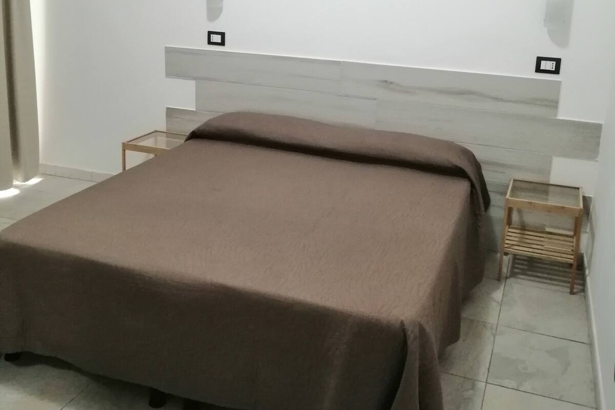 Un dormitorio con cama, mesita de noche y lámpara de pared.