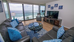 Uma sala de estar moderna com uma televisão grande, sofá de couro e uma mesa de vidro.