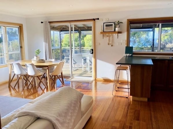 Une chambre moderne comprenant un lit, un coin repas avec des chaises, un coin cuisine avec un comptoir et de grandes fenêtres offrant une vue sur l’extérieur.