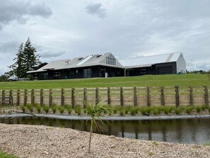 A large building with multiple sections, a grassy area, and a pond. - Large Home great for Families, Work, Groups, Teams (Rukuhia)
