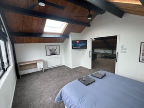 A bedroom with a skylight, a bed, a TV, a radiator, and a bench. - Large Home great for Families, Work, Groups, Teams (Rukuhia)