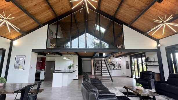 Amplia sala de estar con techo alto, sofás de cuero negro, una mesa de comedor y una escalera que conduce a un nivel superior.
