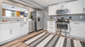 Une cuisine moderne avec des meubles blancs, des appareils en acier inoxydable et un tapis à rayures.