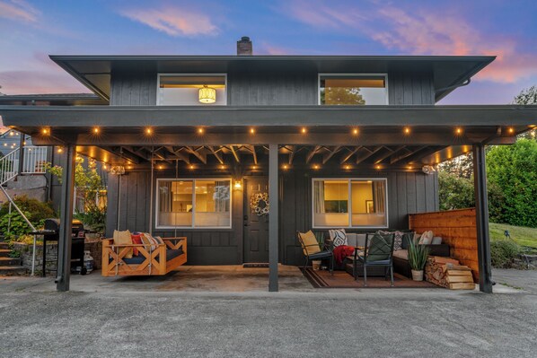Een modern huis met twee verdiepingen, een overdekte veranda, zitplaatsen buiten en een barbecueplek.