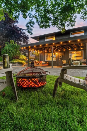 Een modern huis met een overdekt terras, een vuurkorf en een eettafel.