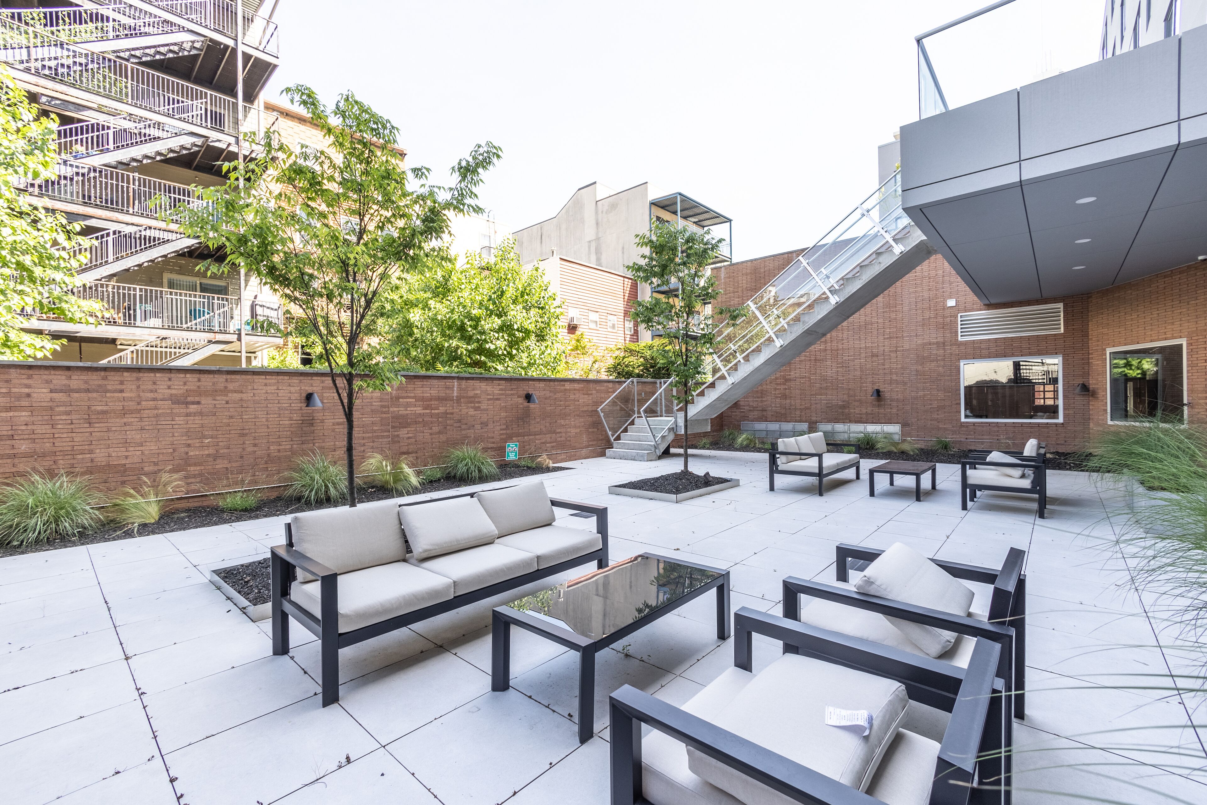 An outdoor patio area with modern furniture, a brick wall, and a staircase leading to an upper level.