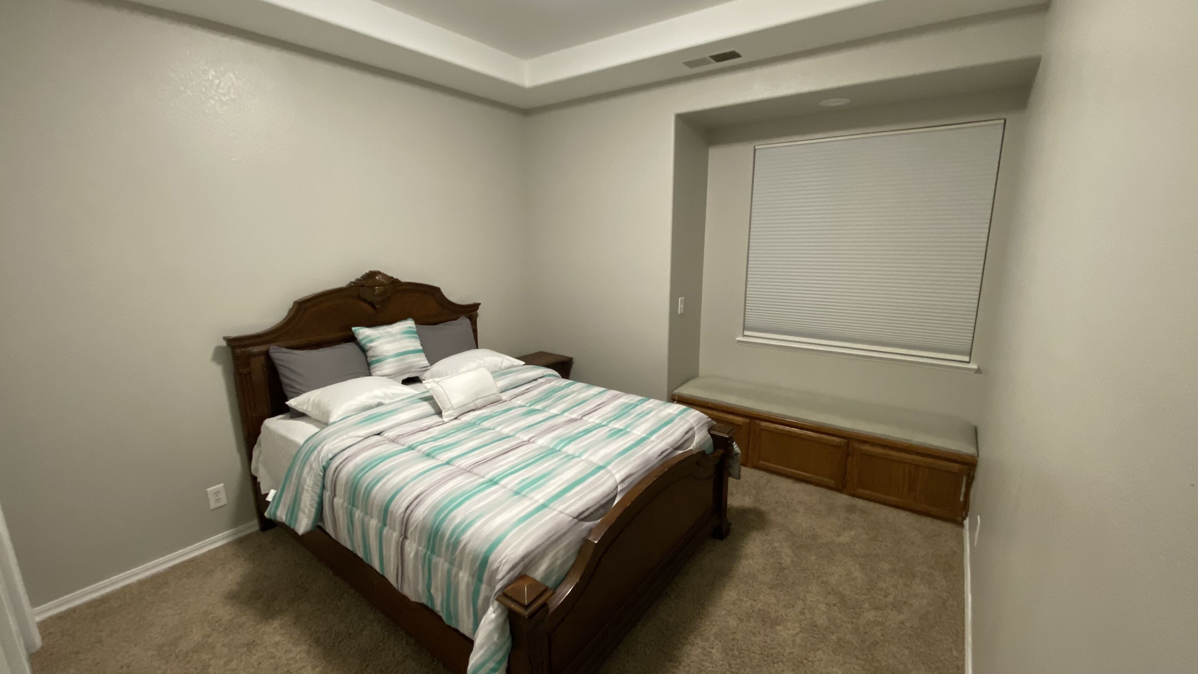 A bedroom with a wooden bed, a window with blinds, and a carpeted floor.