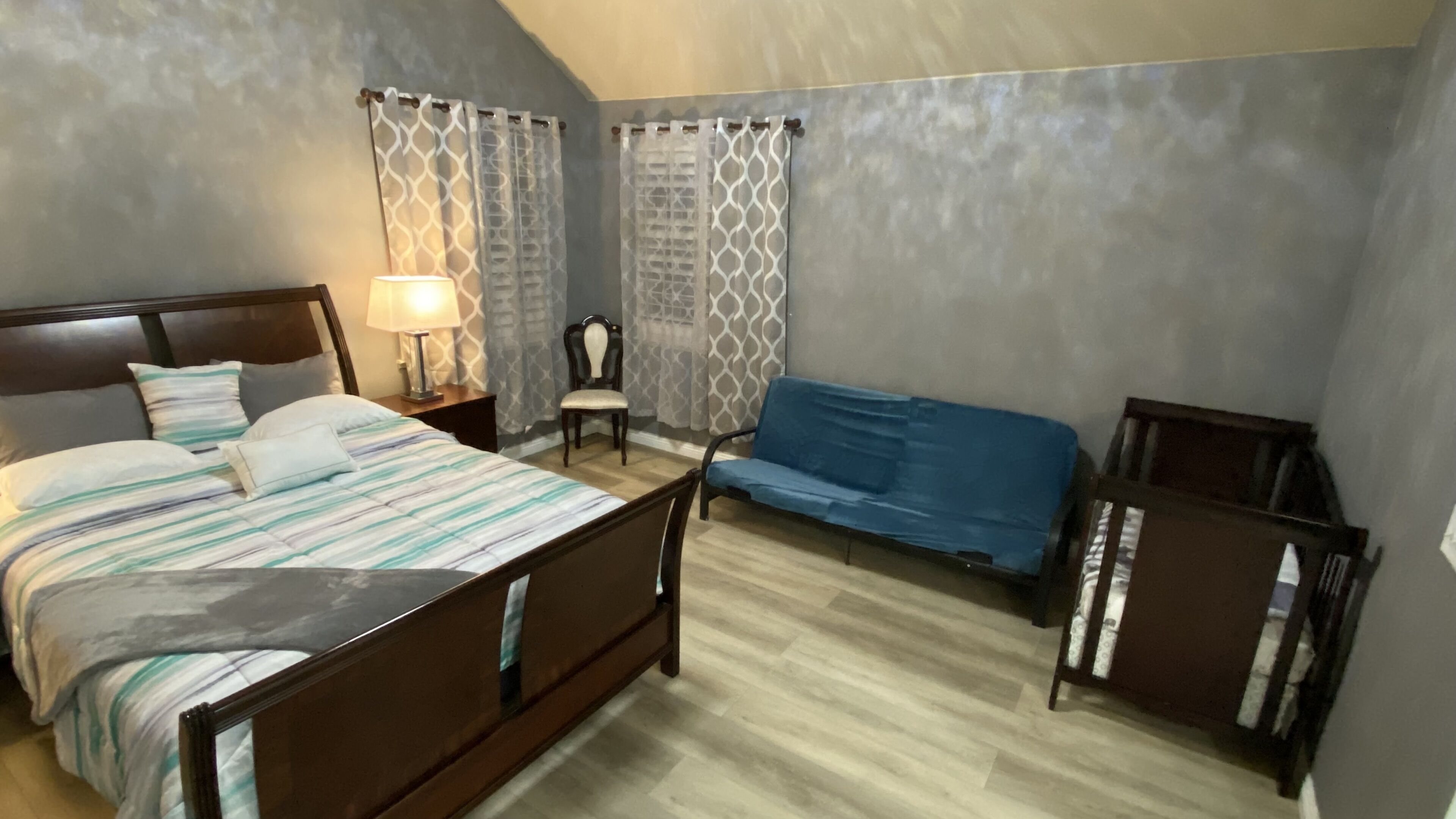 Quarto com cama, poltrona, sofá, mesa de cabeceira e abajur.
