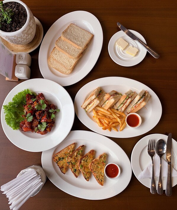 Una mesa servida con diferentes platos, incluyendo sándwiches, papas fritas y una ensalada, junto con salsas y cubiertos.