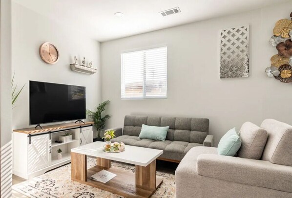 A modern living room with a flat-screen TV, grey sofas, a coffee table, and decorative wall art. - Modern Home Near Disneyland, Beaches, and Little Saigon (Midway City)