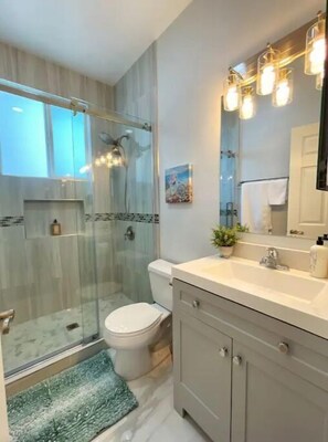 A modern bathroom with a glass shower enclosure, a toilet, a sink with a mirror, and a small potted plant. - Modern Home Near Disneyland, Beaches, and Little Saigon (Midway City)