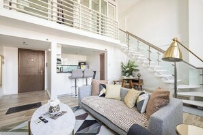 Un salon moderne avec un canapé gris, une table basse ronde et un escalier doté d’une rampe en verre.