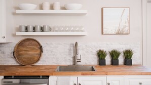 Une cuisine avec des meubles blancs, un plan de travail en bois, un évier en acier inoxydable et trois plantes en pot.