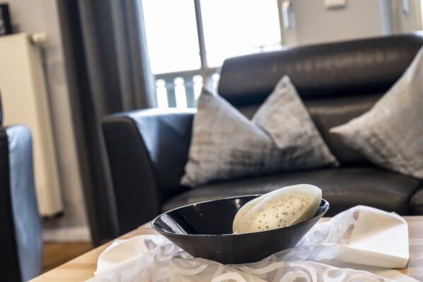 A black bowl on a table with a white cloth, a black tray, and a cushion on a dark leather sofa.