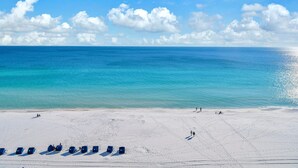 A beach with clear turquoise water, white sand, and a row of blue beach chairs.
