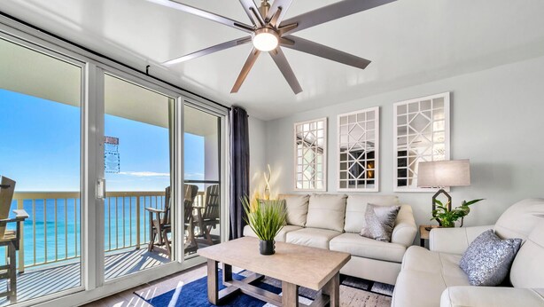 A spacious balcony with a ceiling fan, a sofa, a coffee table, and a view of the ocean.