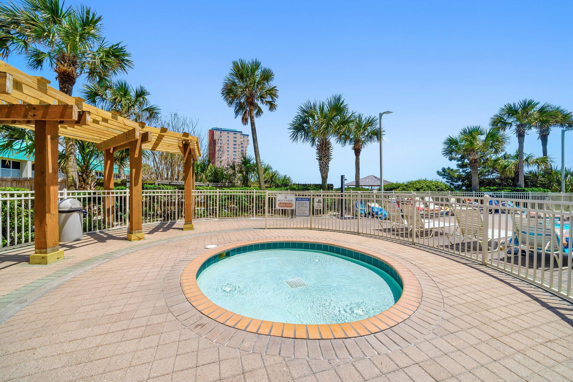 A swimming pool with a wooden pergola and a fenced area.
