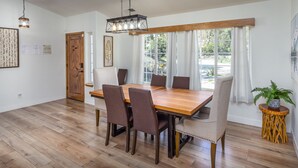 A dining room with a wooden table and six chairs, large windows with white curtains, and a hanging light fixture. - Oasis Riverfront House - Gazebo overlooks the River, 5 miles to Sequoia SNP gate (Three Rivers)
