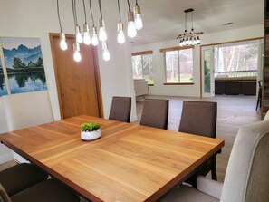 Un espace de salle à manger moderne, avec une table en bois, plusieurs chaises et des luminaires suspendus.