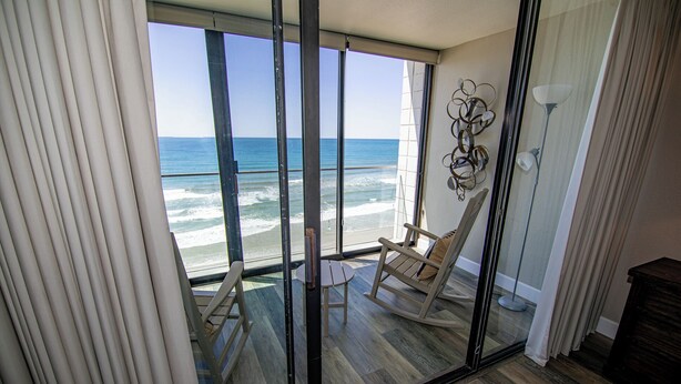 Een balkon met uitzicht op de oceaan, een schommelstoel en een tafeltje.