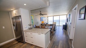Een moderne keuken met een centraal eiland, houten vloeren en uitzicht op de oceaan door grote ramen.