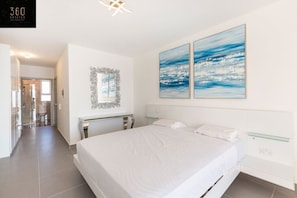 A modern bedroom with a large bed, a desk, and two paintings on the wall. - Duplex seafront APT, in central AREA with Terrace (Saint Paul's Bay)