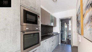 Een moderne keuken met roestvrijstalen apparatuur, grijze keukenkastjes en een betegelde vloer.