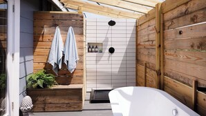 A spa area with a wooden deck, a white bathtub, and a shower with a tiled wall.