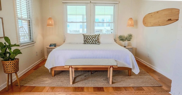 Une chambre à coucher avec un lit, des tables de chevet, une plante en pot et une fenêtre avec des stores.