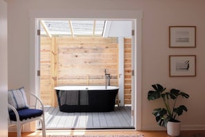 Une salle de bain moderne avec une baignoire sur pieds, une terrasse en bois et une plante en pot.