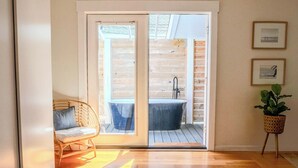 A room with a sliding glass door leading to a balcony with a bathtub and a chair.