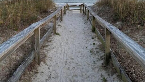 A sandy beach path with wooden railings leading to the ocean.