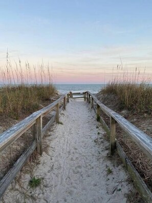 Ein Sandweg am Strand mit Holzwailen, der zum Meer führt.