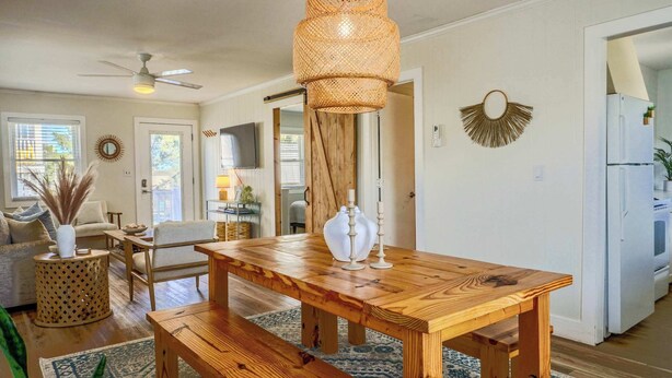 A dining area with a wooden table and benches, a woven light fixture, and a kitchen visible in the background.