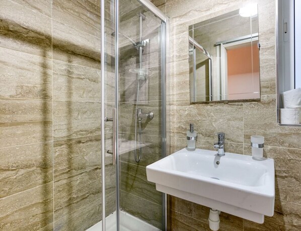 A bathroom with a glass shower enclosure, a white sink with two faucets, and a mirror above the sink. - Gzira, Central APT - Spacious with Super WIFI & AC (Il-Gżira)