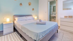 A modern bedroom with a bed, bedside tables, a nightstand, a bathroom with a shower, and a mirror. - Gzira, Central APT - Spacious with Super WIFI & AC (Il-Gżira)
