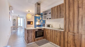 A modern kitchen with wooden cabinets, a built-in oven, and a microwave. There is a dining area with a table and chairs visible in the background. - Gzira, Central APT - Spacious with Super WIFI & AC (Il-Gżira)