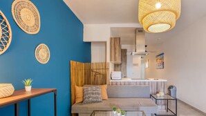 A modern living room with a blue accent wall, a glass coffee table, a sofa, and a kitchen area in the background. - Gzira, Central APT - Spacious with Super WIFI & AC (Il-Gżira)