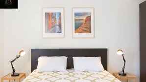 Een hotelkamer met een bed, twee nachtkastjes, twee lampen en twee ingelijste kunstwerken aan de muur.