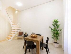 En modern inredning med ett matbord i trä, svarta stolar, en trappa och en krukväxt.