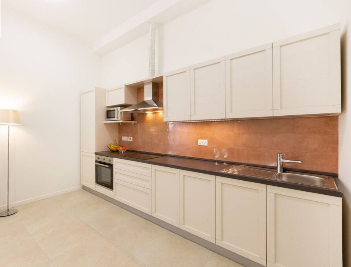 Una cocina moderna con armarios blancos, encimera negra, microondas y pileta de acero inoxidable.