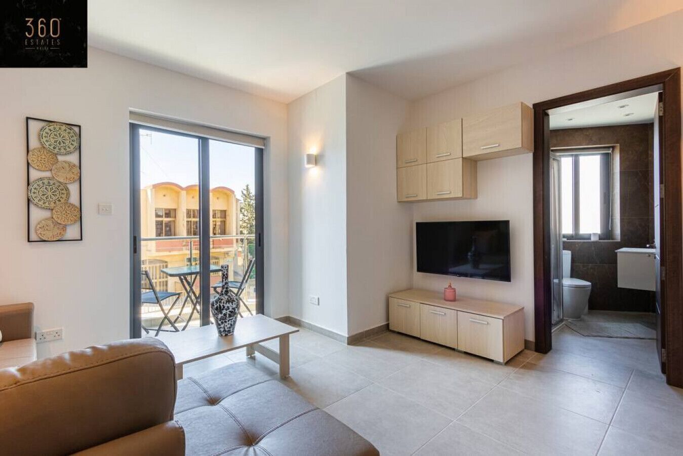 A modern living room with a sofa, a TV on a wooden cabinet, and a balcony with a view of buildings.