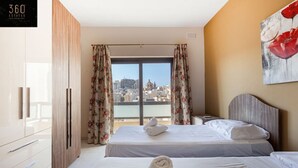 A hotel room with two beds, a city view, and a painting of red flowers. - Sliema Ferries APT, with beautiful views AC & WIFI (Sliema)