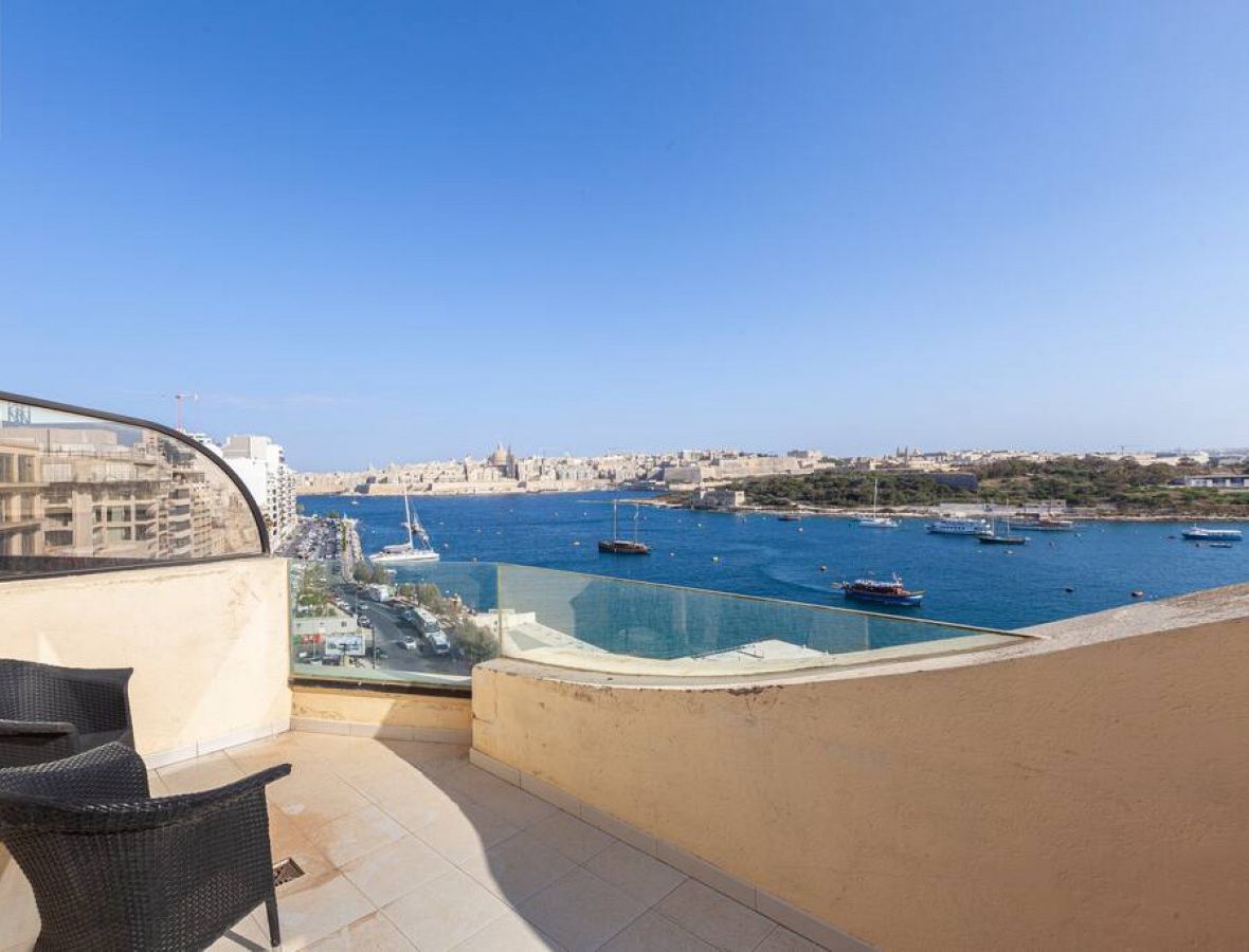 Un balcon offrant une vue sur un port, avec des bateaux et un paysage urbain en arrière-plan.