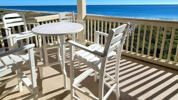 A covered outdoor seating area with a table and chairs, overlooking a beach and ocean. - Oceanfront Lookout, pet friendly with pool (Carolina Beach)